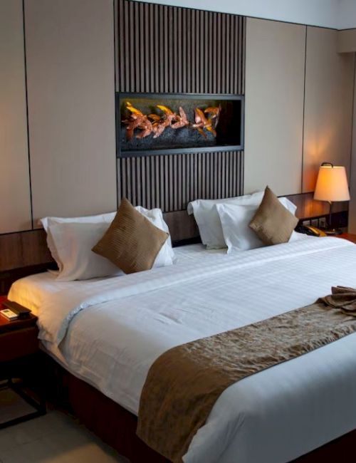 The image displays a cozy hotel room with a large neatly made bed, two bedside tables with lamps, and a wall-mounted decorative feature above the bed.