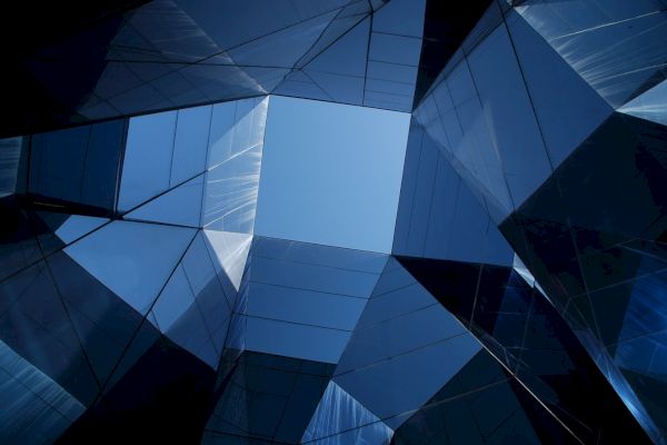 The image shows a geometric architectural structure made of reflective glass panels with a view of the sky in the center.