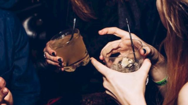People are holding drinks and laughing in a social setting, indicating a lively, festive atmosphere.