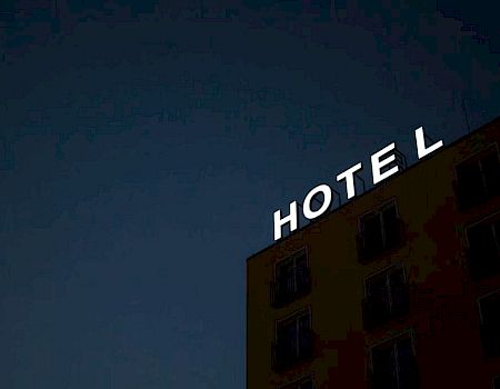 The image shows the side of a building at dusk with a sign that reads "HOTEL" in bright white letters against a dark sky.