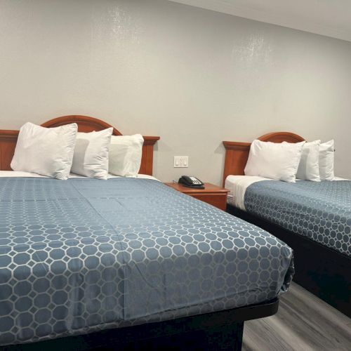 The image shows a hotel room with two neatly made beds, blue patterned bedding, white pillows, and a nightstand with a phone in between them.