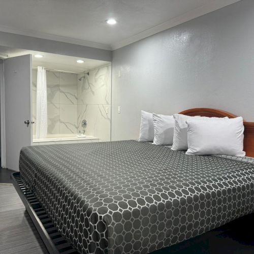 The image shows a hotel room with a neatly made bed, two pillows, and an open door revealing a bathroom with a tub.