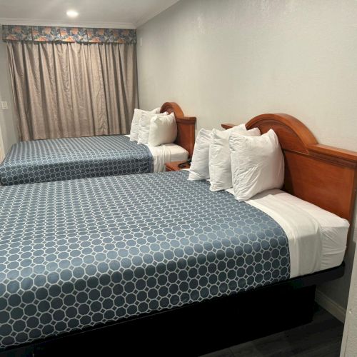 The image shows a hotel room with two neatly made beds, each with blue and white patterned bedspreads, white pillows, and wooden headboards.