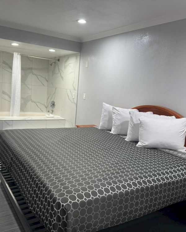 A modern hotel room with a large bed, white sheets, a wooden headboard, and a corner bathtub near a white door.