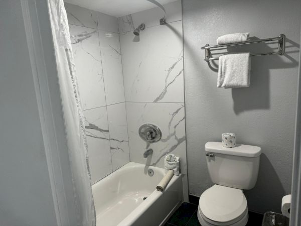 This image shows a bathroom with a bathtub, a showerhead, a toilet, and a towel rack holding folded towels above the toilet, always ending the sentence.