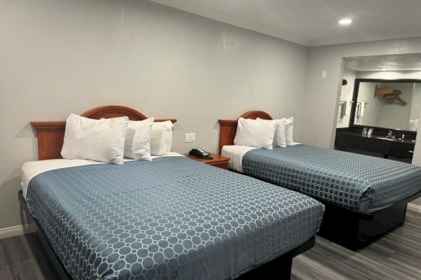 The image shows a hotel room with two double beds adorned with blue bedding. There are pillows on each bed, and a small nightstand in between.