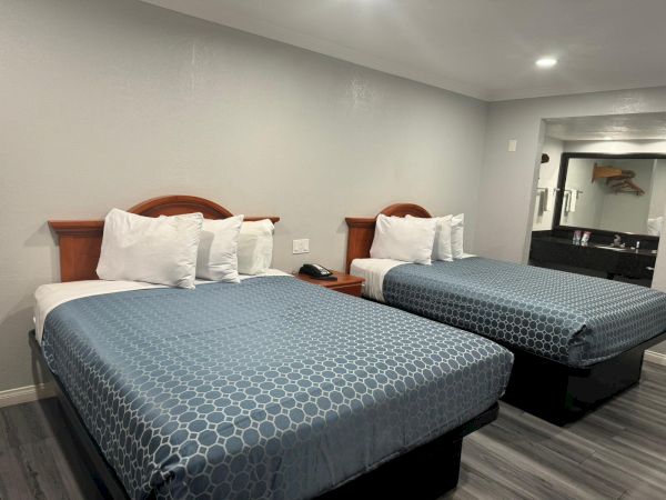The image shows a hotel room with two double beds adorned with blue bedding. There are pillows on each bed, and a small nightstand in between.