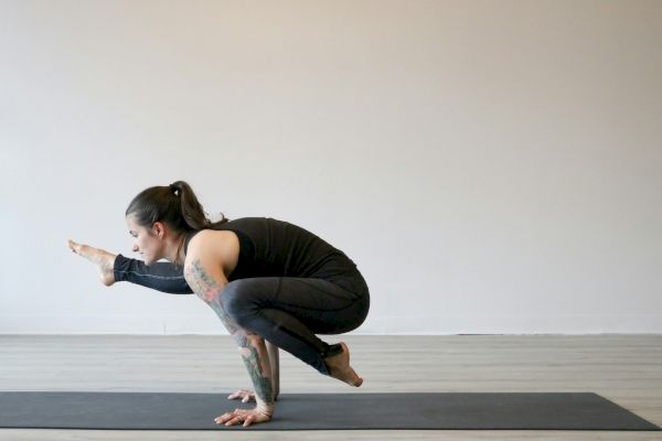 A person is performing a yoga pose on a mat, balancing on their hands with one leg extended forward and the other bent.