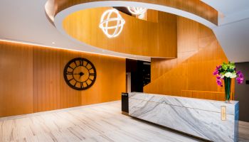 A modern reception area with a marble desk, a large wall clock, wooden design elements, and decorative lighting, flowers on the counter.
