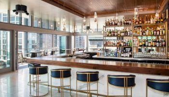 This image shows a sophisticated bar with high-end seating, a wooden counter, and a well-stocked liquor shelf in a modern setting.