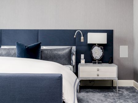 A modern bedroom with a blue and white color scheme. It has a bed with blue pillows, a nightstand, a lamp, and a wall-mounted reading light ending the sentence.
