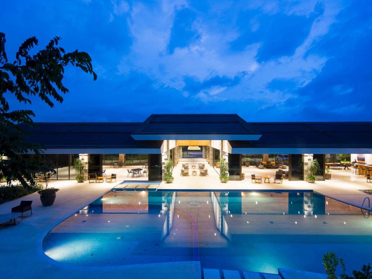 A luxurious open-air pool area at night, illuminated with blue lighting, showcasing a modern building and surrounding lounge areas.
