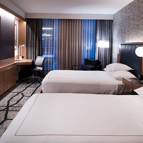 The image shows a modern hotel room with two neatly made beds, a work desk, a TV on the wall, and contemporary decor ending the sentence.